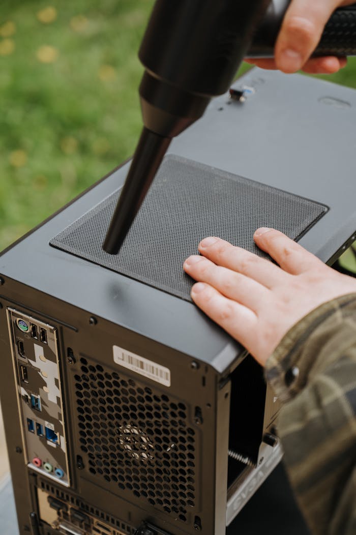 Person cleaning PC case with an electric duster to prevent dust buildup and ensure efficient airflow.